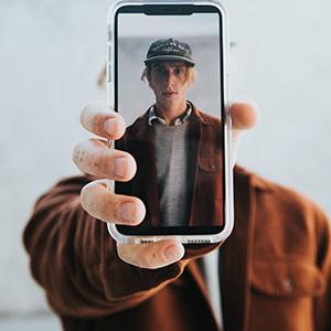 Photo d'un home tenant un téléphone portable à bout de bras devant son visage.