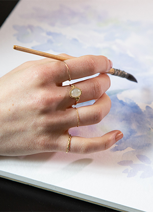 Photo d'une main tenant un pinceau au dessus d'un toile à l'aquarelle.